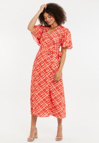 Rot-karierte Wickelkleid in Orange und Rot mit kurzen, puffigen Ärmeln; verfügt über eine taillierte Bindung und einen fließenden, knielangen Rock. Glatter Stoff.