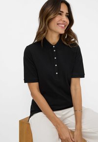 Sort polo shirt med korte ærmer, knaplukning foran og klassisk krave; glat tekstur; parret med lyse bukser.