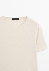 T-shirt beige a girocollo realizzato in un tessuto morbido. Presenta maniche corte e un orlo dritto. Etichetta visibile all'altezza del collo che ne aumenta l'identità.