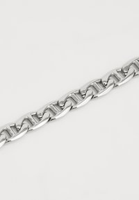 Bracelet en métal argenté avec des maillons entrelacés, finition polie et légère courbure dans le design. Texture lisse.
