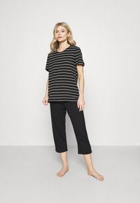 T-shirt a righe bianche e nere con maniche corte abbinato a pantaloni cropped neri. Entrambi i capi sono realizzati in un tessuto morbido e leggero.