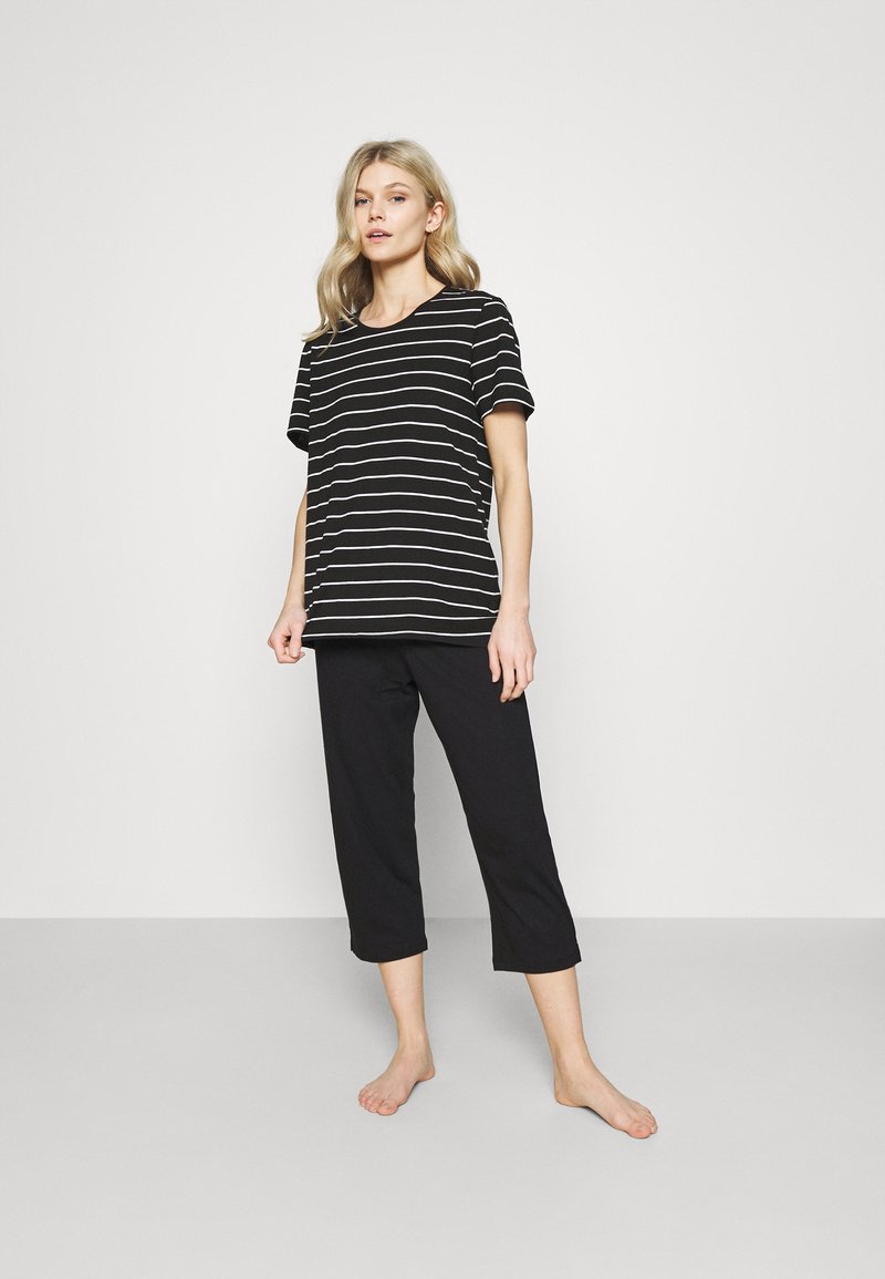 T-shirt a righe bianche e nere con maniche corte abbinato a pantaloni cropped neri. Entrambi i capi sono realizzati in un tessuto morbido e leggero.