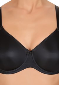 Donna che indossa un reggiseno nero liscio con ferretto, spalline regolabili e un piccolo fiocco decorativo al centro davanti.