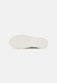 Semelle d'une chaussure blanche Calvin Klein avec un motif texturé de cercles et de X, et le nom de la marque embossé au centre.