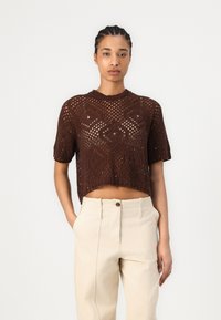 Top corto a maglia marrone con un motivo testurizzato, maniche corte e scollo rotondo, abbinato a pantaloni beige chiaro a vita alta.