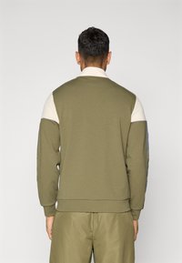 Olijfgroene sweater met een witte kraag, met geruite accenten op de mouwen en geribbelde manchetten. Soepele stof met een losse pasvorm.