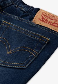 Temno modre denim hlače z vidnimi rumenimi šivi, z zadnjim žepom in usnjeno etiketo z napisom "Levi Strauss & Co."