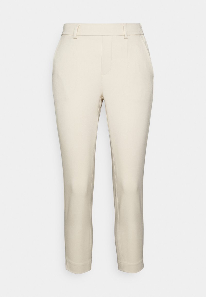 Beżowe dopasowane spodnie o prostym kroju, z mankietami z przodu i bezszwami kieszeniami bocznymi. Gładka faktura materiału bez widocznych wzorów.