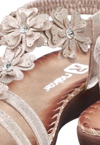 Gros plan sur une sandale beige ornée de fleurs en tissu avec des centres en strass, dotée d'une semelle intérieure rembourrée avec des coutures visibles.