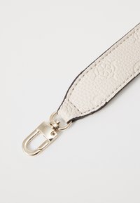 Cintura in pelle di un crema chiaro con superficie testurizzata, caratterizzata da un bordo scuro a contrasto e una chiusura in metallo dorato per il fissaggio.