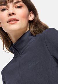 Marine fleece pullover met hoge kraag, kwart-rits sluiting en reliëflogo. Zachte textuur, gladde afwerking en getailleerd ontwerp.