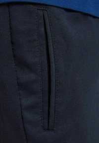 Granatowe dresy z tkaniny z boczną kieszenią z eleganckim, ukrytym zamkiem błyskawicznym. Tekstura jest gładka z subtelnym, tkanym wzorem.