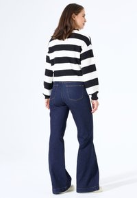 Gestreifter weißer und schwarzer Strickpullover mit langen Ärmeln, kombiniert mit dunkelblauen ausgestellten Jeans, die ein klassisches Rückentaschendesign aufweisen.