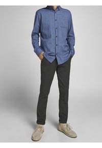 Blå skjorta med knäppning i strukturerad tyg, med en bröstficka, i kombination med mörkgrå avsmalnande byxor och beige mocka ankelstövlar.