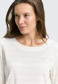 Haut à manches longues beige clair avec un col large, affichant de fines rayures horizontales et une texture douce. Idéal pour une tenue décontractée.