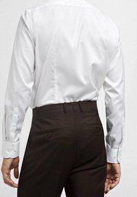 Witte langslavende shirt met knoopmanchetten, gecombineerd met donkerbruine broeken met platte zakken en een gladde textuur.