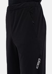 Black athletic pants made of lightweight fabric, featuring a slim fit, elastic waistband, side pocket, and a reflective logo on the leg.