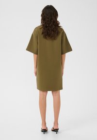 Olivově zelené oversized šaty s krátkými rukávy, ke kolenům, vyrobené z měkké tkaniny, s rovnými liniemi a minimalistickým designem.