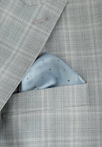 Helles graues Sakko mit einem strukturierten Muster. Ein blauer Seideneinstecktuch mit diagonalen Streifen und kleinen silbernen Punkten ist in der Tasche präsentiert.