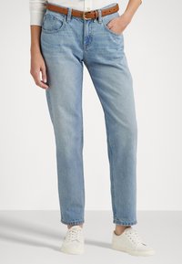 Lichtblauwe denim jeans met een rechte pijp, hoge taille en een bruine leren riem. Draag ze met witte sneakers. Eenvoudige stikseldetails.