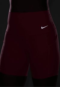 Burgundowe szorty z wysokim stanem wykonane z elastycznego materiału, z małym białym logo Nike na pasie i kieszeniami po bokach.