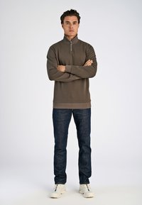 Dark grey long-sleeve pullover with a high collar and zipper, paired with blue jeans and light-colored sneakers. Simple, minimalistic design.