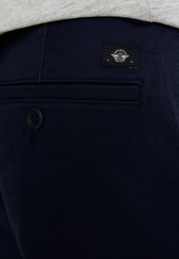 Pantalon bleu marine en tissu texturé, avec une poche arrière, une étiquette noire avec le logo et une fermeture à bouton noir.
