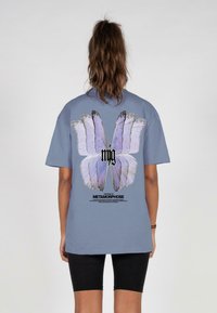 Light blue cotton t-shirt featuring a large, colorful butterfly design on the back with text reading "THE STORY OF METAMORPHOSE."