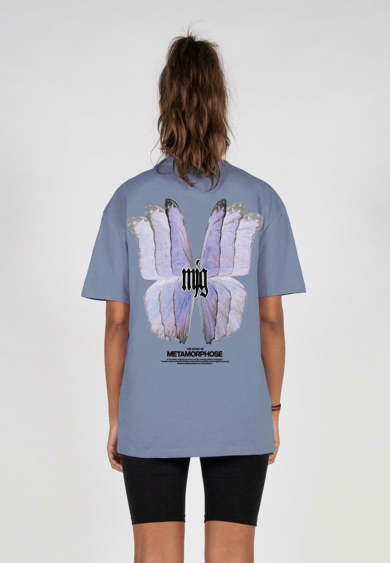 Lyseblå bomulds t-shirt med et stort, farverigt sommerfugledesign på ryggen med teksten "Historien om metamorfose."