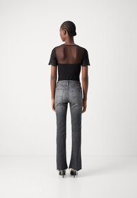 Haut noir ajusté avec un dos transparent à pois et des manches en dentelle, associé à un jean flare gris avec un ourlet effiloché et des poches arrière.