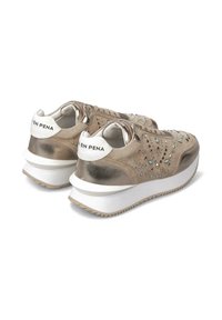 Zapatillas deportivas con acabado de ante beige y metálico, adornadas con tachuelas plateadas, presentan una suela de goma blanca y una tira de agarre de contraste.