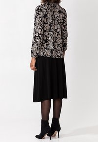 Blusa nera a maniche lunghe con motivo floreale, design con schiena arricciata; abbinata a una gonna nera fino al ginocchio e stivali neri con tacco.