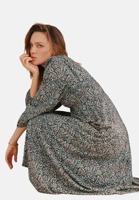 Langes Blumenkleid mit langen Ärmeln, das einen dunklen Hintergrund mit rosa und türkisfarbenen Blättermustern zeigt, aus leichtem Stoff gefertigt und mit fließendem Design.