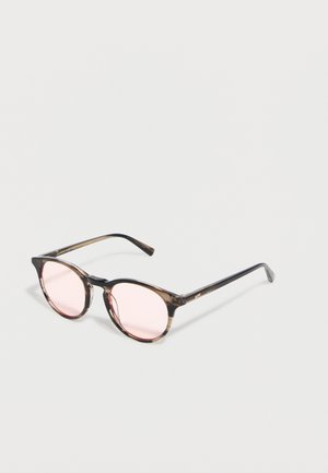 Kulaté brýle s tenkými průhlednými hnědými obroučkami a světle růžovými čočkami ležící na bílém povrchu.