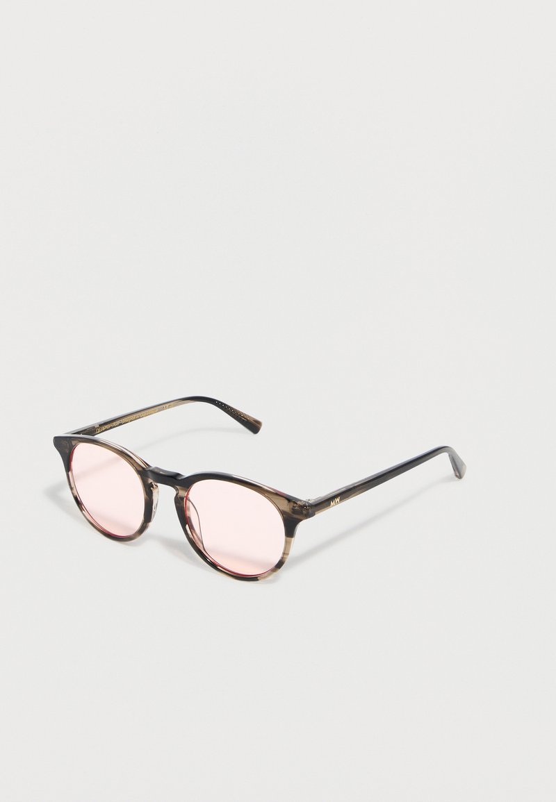 Στρογγυλά γυαλιά με λεπτά, ημιδιαφανή καφέ σκελετούς και φακούς σε ανοιχτό ροζ χρώμα, τοποθετημένα πάνω σε λευκή επιφάνεια.