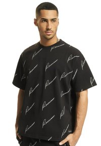 Juodas trumpomis rankovėmis marškinėliai su laisvu pjūviu, puikiai tinka, su pakartotu baltu "Rocawear" tekstu kursyvine šriftu. Glotni medvilnės tekstūra, kasdieniškas dizainas.