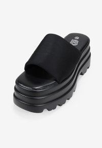 Sandalias de plataforma negras con una amplia correa de tela y una suela gruesa y texturizada. Plantilla suave con un pequeño logotipo en la parte superior.