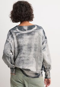 Sudadera de gran tamaño en un estampado negro y gris deslavado. Tejido suave con hombros caídos y puños de canalé, combinando con jeans verdes.