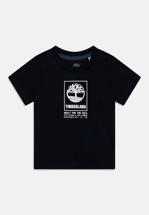 T-shirt noir à manches courtes en coton, avec un logo Timberland imprimé en blanc, accompagné de texte et d'un design d'arbre. Boutons-pression sur l'épaule.
