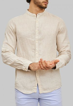 Chemise longue beige clair à manches longues avec col montant, fermeture à boutons, et tissu texturé. Comprend des poignets à boutons et une coupe ajustée.