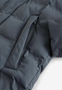 Detail einer schwarzen Pufferjacke mit einer Reißverschlusstasche, glatter Textur, gesteppter Musterung und schrägem Ärmeldesign.