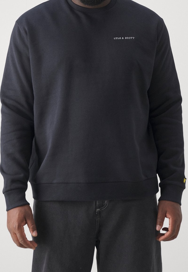 Námořnická crewneck mikina vyrobená z bavlněné směsi, s malým bílým logem na hrudi a žlutým akcentem na rukávu.