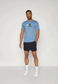 Šviesiai mėlynas trumpas rankovės marškinėlis su "new balance" logotipu, juodos šortai, balti sportbačiai ir balti kojinės; lygi medžiaga ir sportiškas siuvimas.