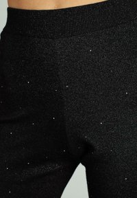 Leggings negros elásticos que presentan una cinturilla acanalada y chispas plateadas dispersas, añadiendo textura e interés visual a la tela.