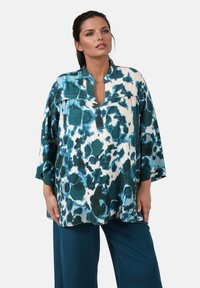 Langärmlige Bluse in Teal und Weiß mit einem Aquarell-Blumenmuster, ausgestattet mit einem Stehkragen und einem Schlüsselaugen-Ausschnitt.