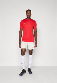 Crvena atletska majica s crnim detaljima, bijele kratke hlače, bijele čarape i crne nogometne kopačke. Nike logotipi na majici i hlačama.
