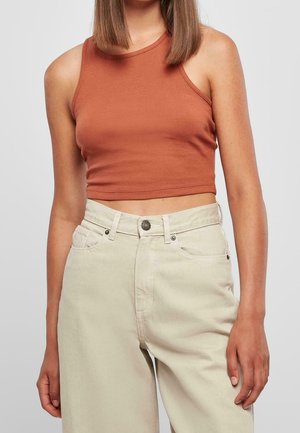 Femme portant un crop top sans manches couleur rouille et un pantalon taille haute beige clair avec poches et fermeture à boutons.