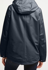 Mörkblå vattentät jacka med huva, med en slät yta, tryckknappar vid handlederna och en något längre bakre fåll.