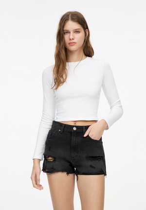 Biely dlhý rukáv crop top skombinovaný s čiernymi denimovými šortkami s vysokým pásom, ktoré majú vyblednuté detaily a roztrhnuté okraje.