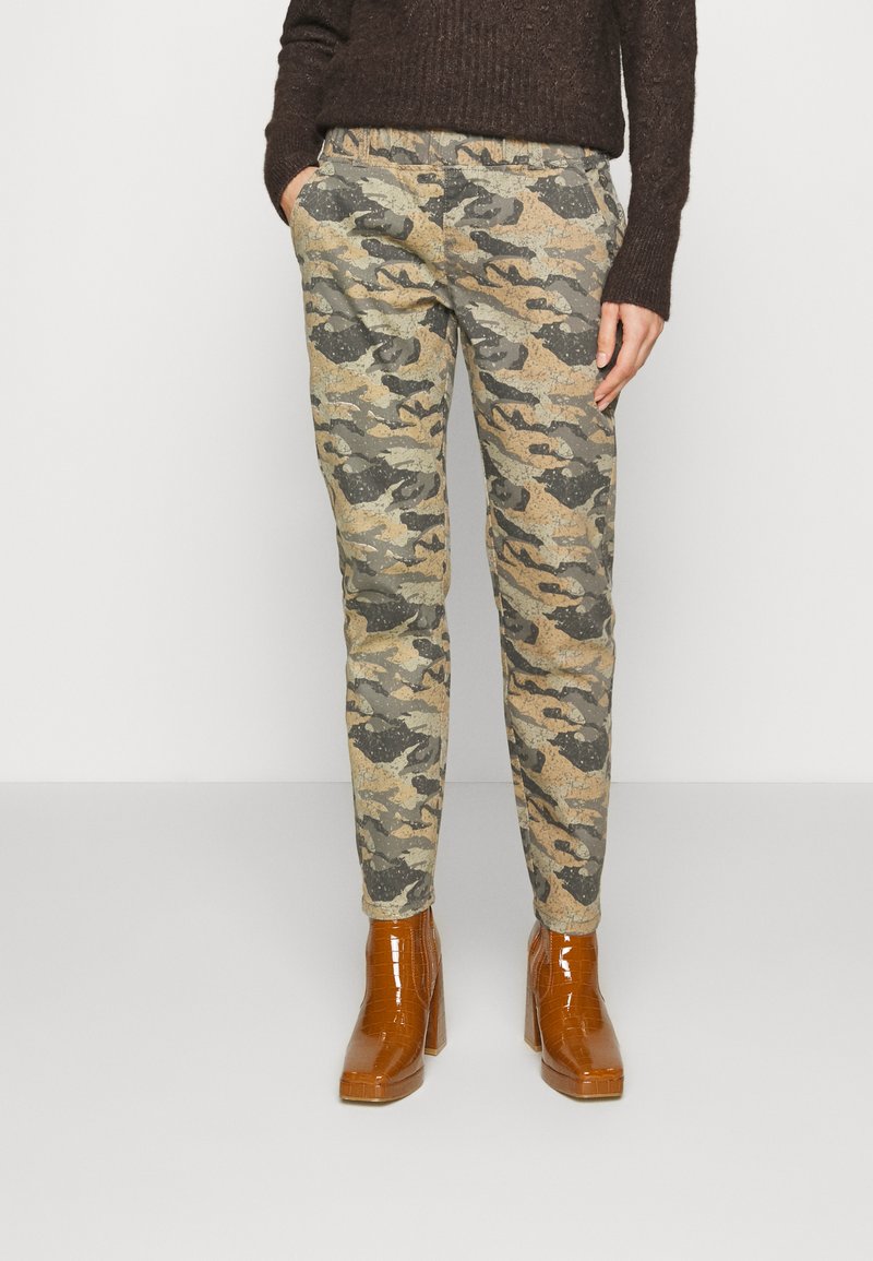 Calças com padrão camuflado em tons de verde e castanho suaves, apresentando uma cintura confortável e bolsos laterais, acompanhadas de botas de salto castanhas brilhantes.